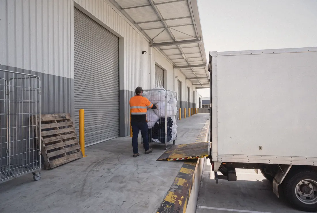A worker in SB Empire colours wheels bagged linen and uniforms from a distribution centre dock to a truck