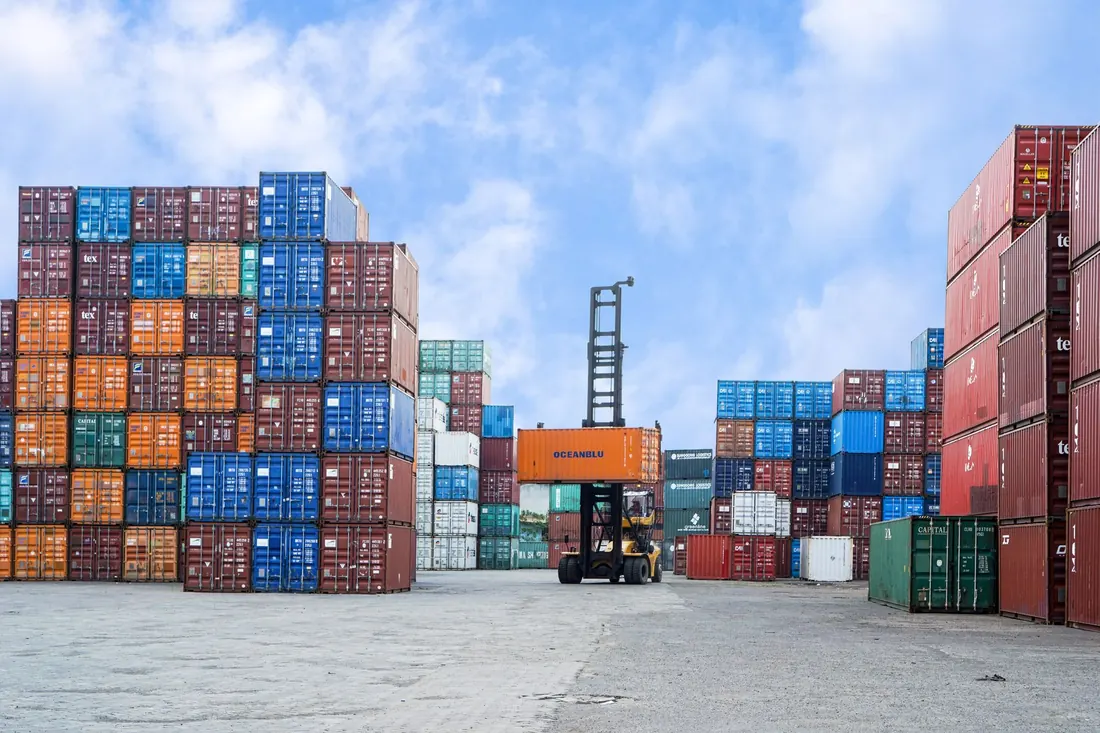 Stacked shipping containers in a container yard, with a container forklift lifting a box